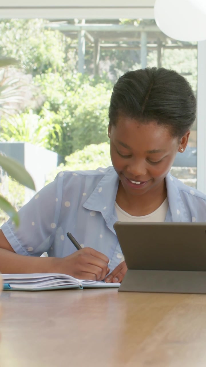 Vertical video: Studying teen girl writing notes at table, deadline pushing, with tablet and pen