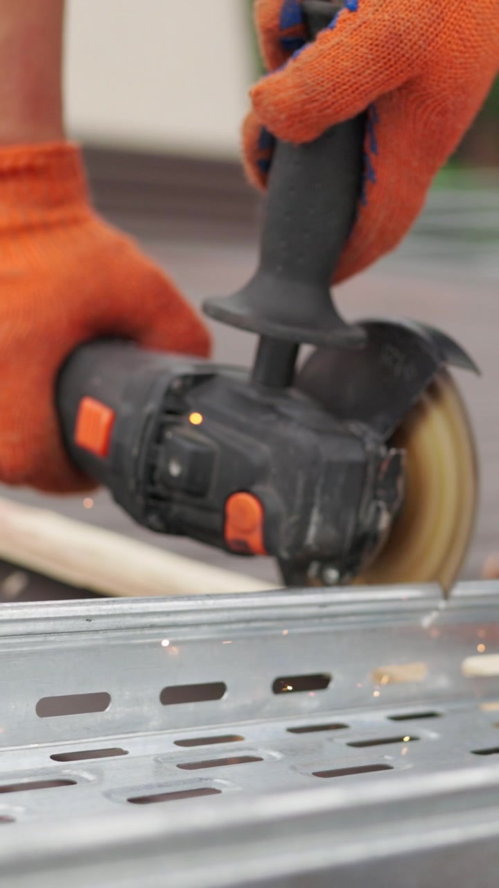 A closeup shot of a person using an angle grinder to cut through metal wearing orange work gloves