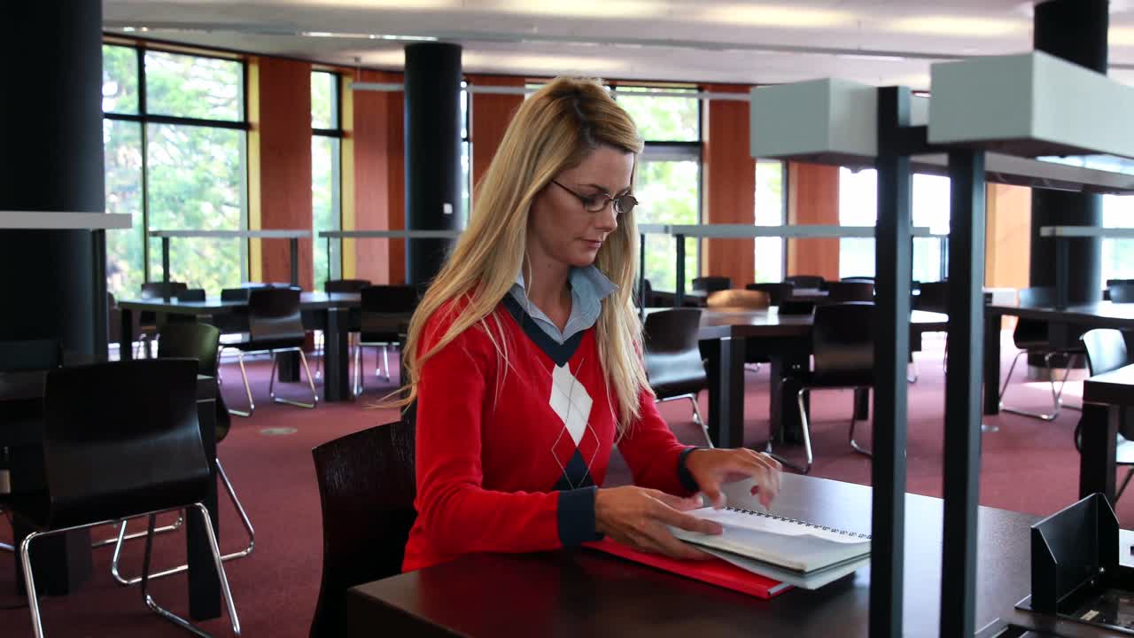 Mature student with reading glasses studying at library desk