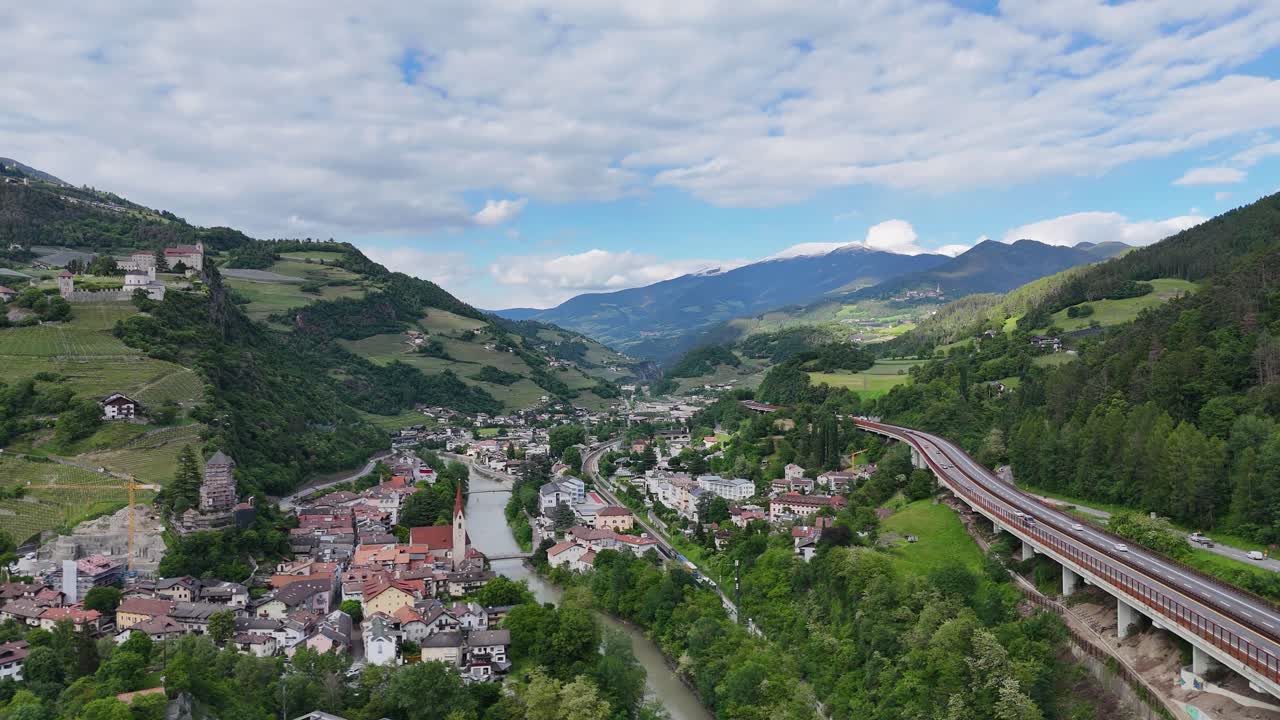 Drone footage captures Monastero di Sabo in Italy, with a valley, small town, river, winding roads, and mountains, showcasing natural beauty and historical charm