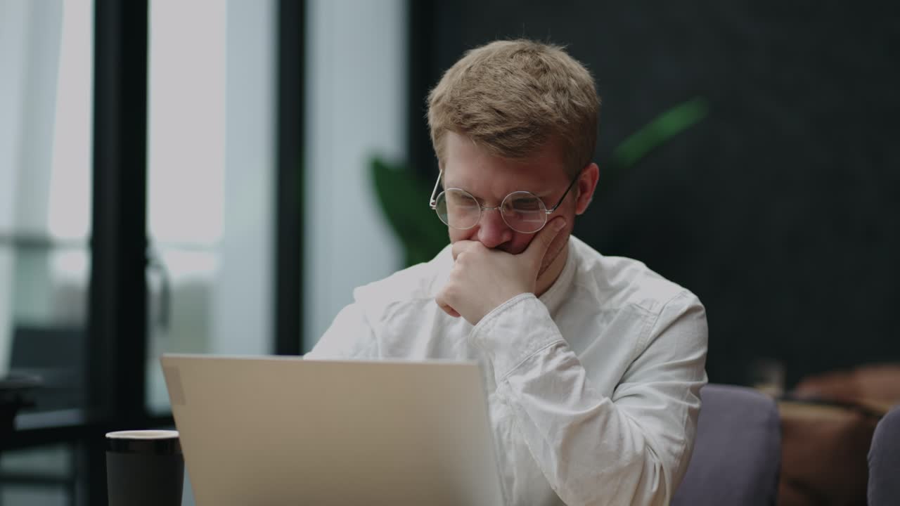 frustrated and annoyed man with glasses is reading news in internet, looking at display of laptop