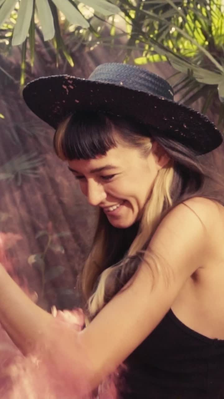 Young smiling caucasian woman with red smoke bomb and dancing stands in park