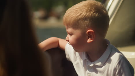 thoughtful little boy looks at river from sailing motorboat salon closeup. cute toddler child leans on bench back travelling by vessel on vacation