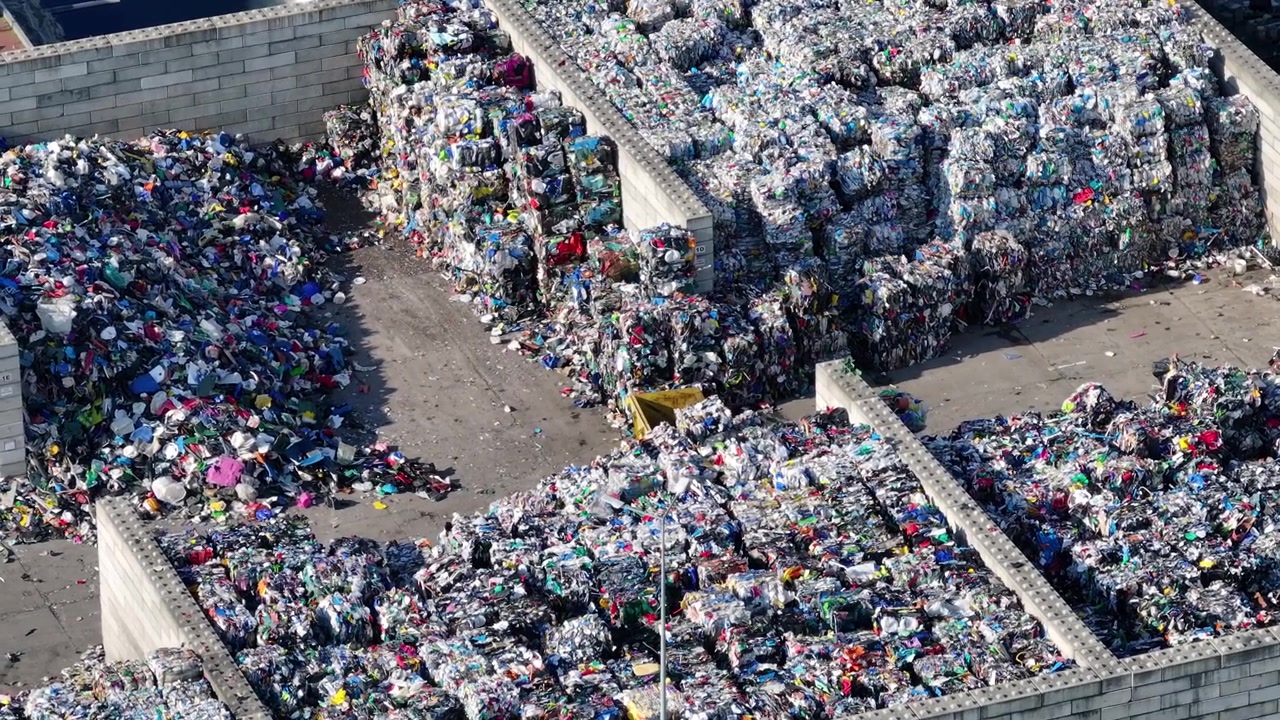 I rifiuti di plastica sono accatastati in pile in un impianto di riciclaggio. I lavoratori smistano i materiali per la lavorazione. Le attrezzature operano per separare e recuperare le risorse riciclabili.