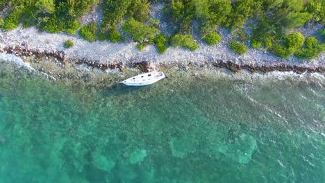 a shipwrecked boat on a tropical shore with clear, turquoise water, overhead backward spinning aerial