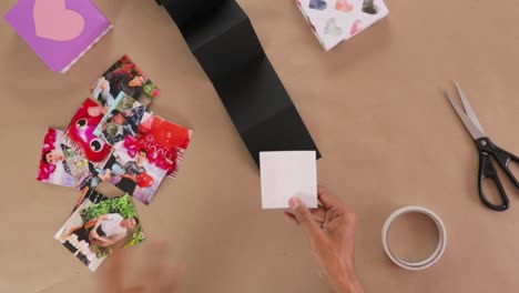 hands assembling photo gift for valentines day using black paper strip, photos, and tape