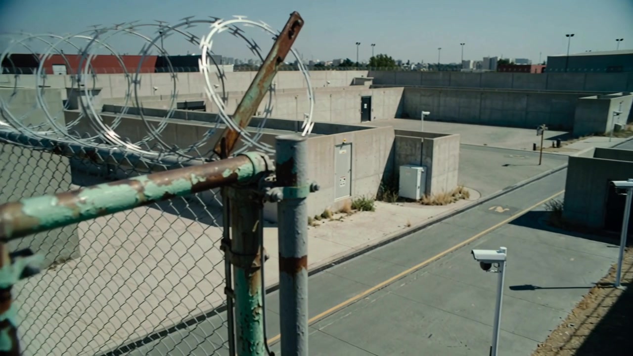 Panning camera starting, showing rusted chainlink post with razor wire at compound left, copy space