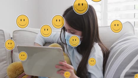 Animation-Digitaler-Emoji-Symbole-über-Einem-Kaukasischen-Mädchen-Mit-Gesichtsmaske,-Das-Zu-Hause-Ein-Tablet-Verwendet
