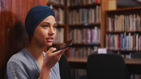 Asian-female-student-wearing-a-blue-hijab-sitting-and-using-a-smartphone