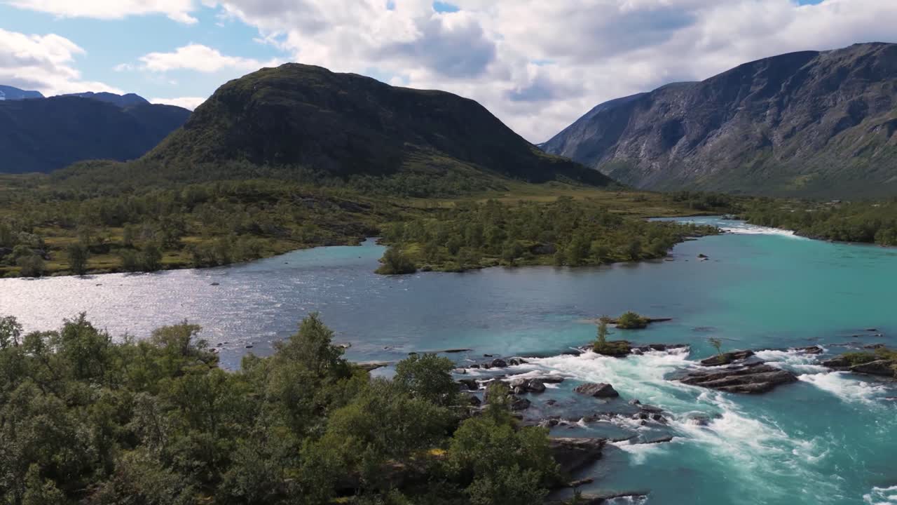 Beautiful aerial view capturing the lush Norwegian landscape, featuring mountains, clear rivers, and dense green forests under a partly cloudy sky.