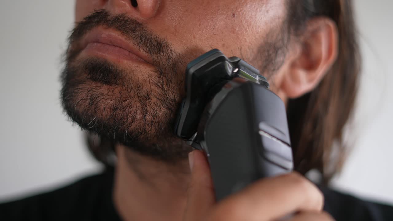 Latinský muž si zastřihuje vousy a knír elektrickým holicím strojkem, brada