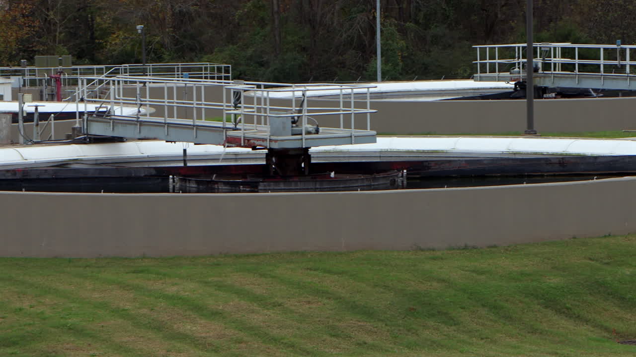 Wide view of clarifier basins at a wastewater treatment plant, settling and treating processed sewage water in a structured, industrial system - panning from left to right
