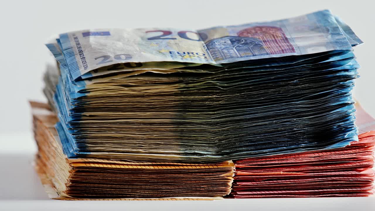 Velké stohy bankovek v hodnotě 5 €, 10 €, 20 € a 50 € se plynule otáčejí na bílém povrchu