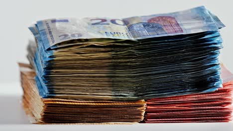 big stacks of €5, €10, €20, and €50 banknotes rotate smoothly on a white surface