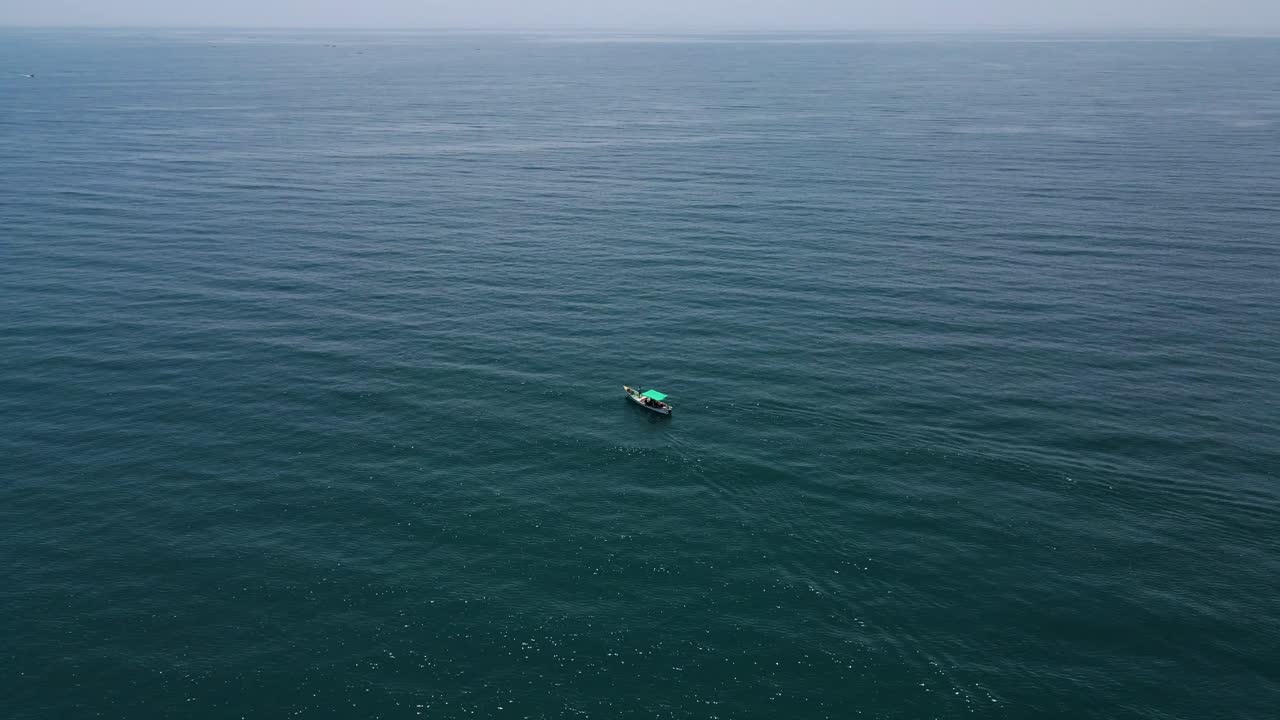 Aerial drone shot focusing on a fishing boat dwarfed by the vast and boundless ocean around it.