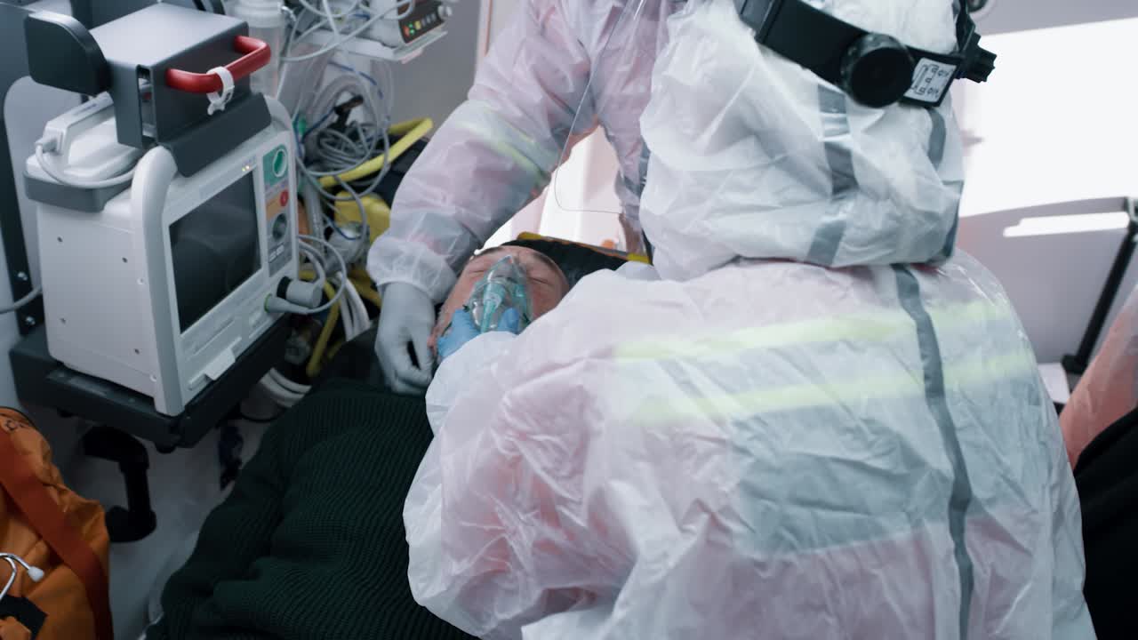 doctors Putting Respirator on Man with Pneumonia from above Paramedics in Hazmat Suits Putting Oxygen Mask on Suffocating Elderly Patient while Working in Emergency Medicine Vehicle during Pandemic