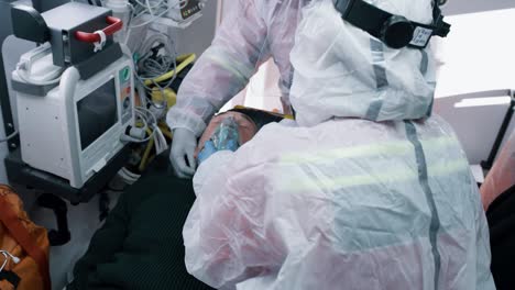 doctors putting respirator on man with pneumonia from above paramedics in hazmat suits putting oxygen mask on suffocating elderly patient while working in emergency medicine vehicle during pandemic