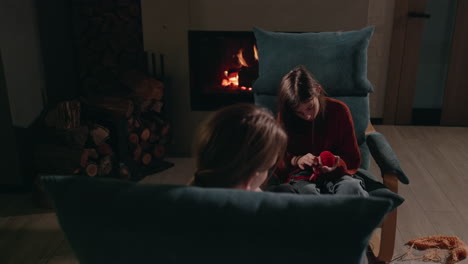 two girls knitting by the fireplace