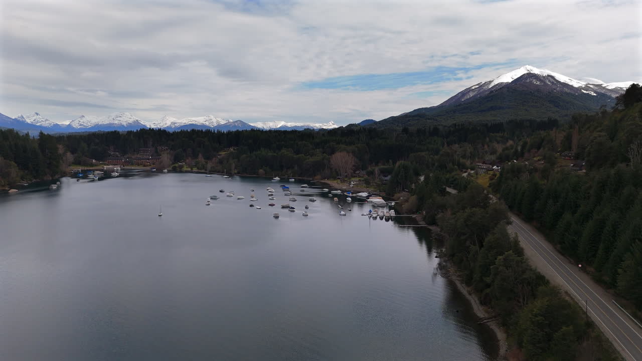 drone de seguimiento hacia adelante disparado sobre el puerto deportivo en villa la angostura, argentina. cielo nublado, lago tranquilo y montañas nevadas. disparado 4k-60fps