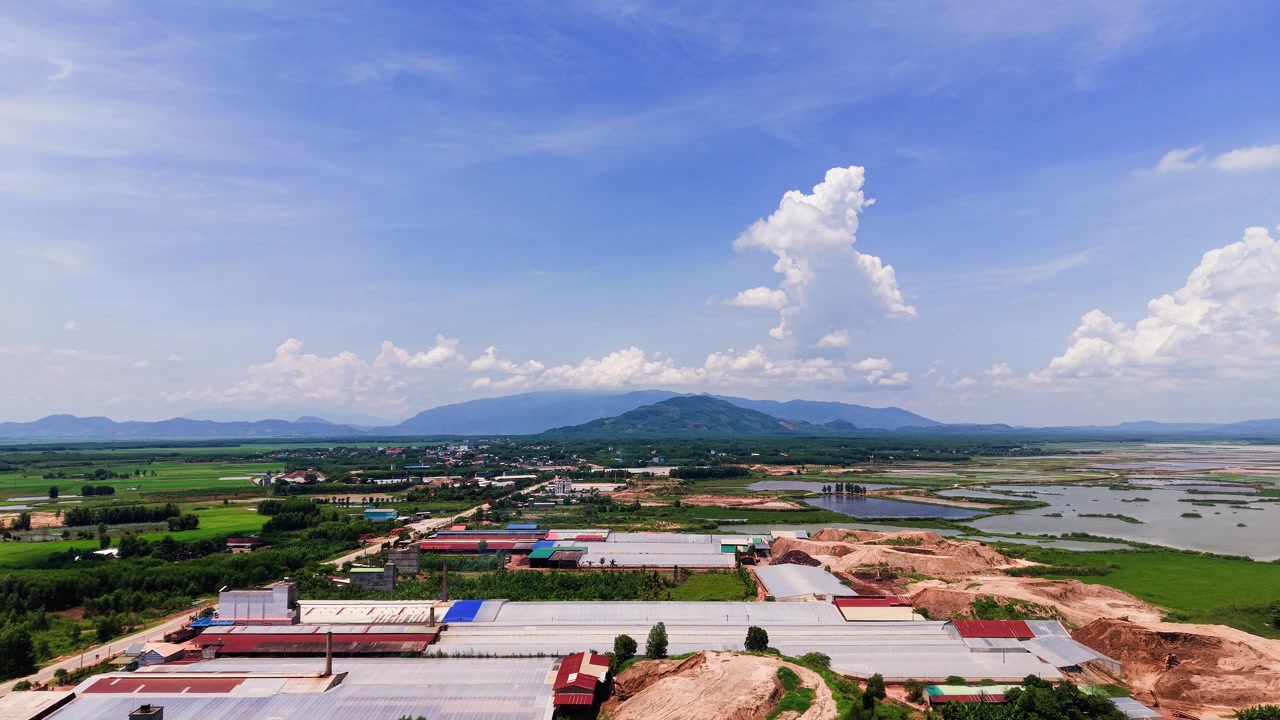 Duc Linh exibe vastos campos e edifícios sob um céu azul claro. Colinas verdes são visíveis ao fundo. É um dia ensolarado em Lam Dong, Vietnã, com paisagens abertas.