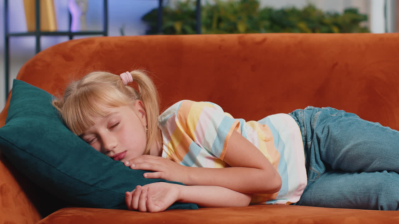 Tired school girl child kid lying down in bed taking a rest at home napping falling asleep on sofa
