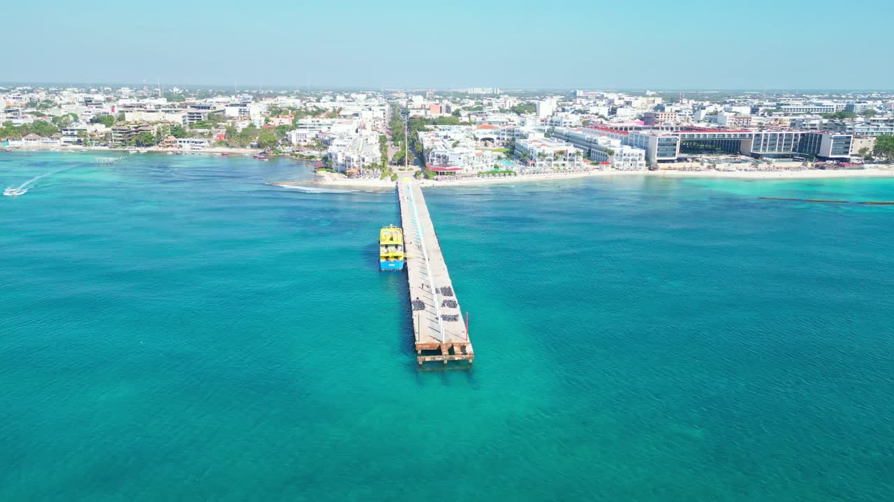 Long pier stretching into the turquoise waters, with the city skyline of Playa del Carmen in the background