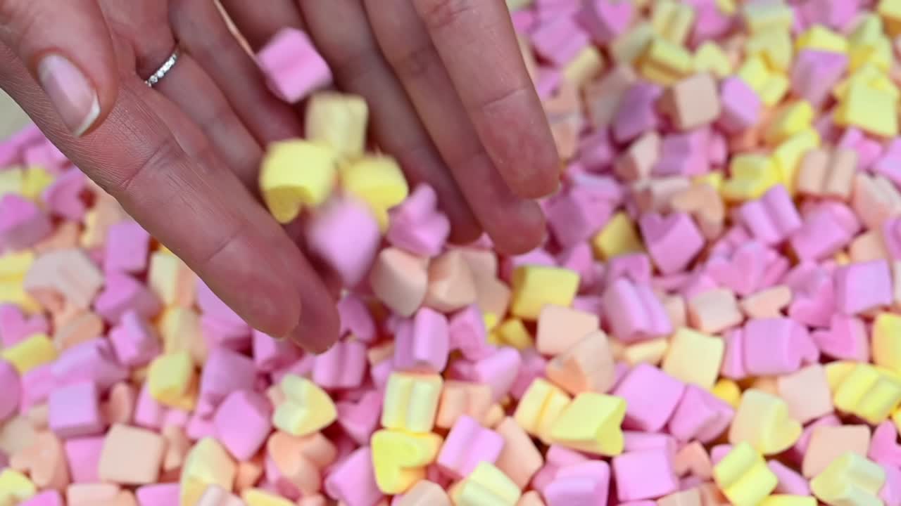 Woman hands throw from the hands several multicolored heart shaped marshmallow. Overhead shot. Close up. Slow motion