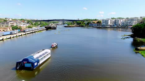 Interceptor-004-cleaning-polluted-river-in-Dominican-Republic,-brown-waters-bridge-in-the-background