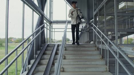 hombre llevando una bicicleta por escaleras de metal