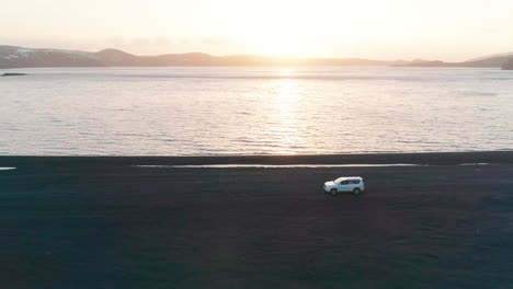 vehicle travelling across lake kleifarvatn black sand beach on journey across icelandic sunset landscape