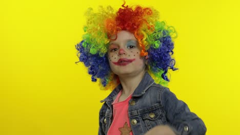 una niña payasa con una peluca colorida haciendo caras tontas. divirtiéndose, sonriendo, bailando. halloween