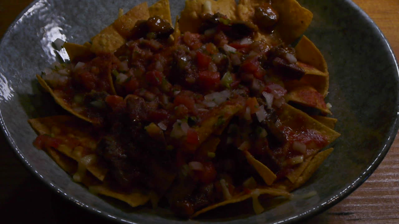 plato de nachos cubierto con salsa picante y carne picada, filmado de cerca con un ligero movimiento para revelar el plato