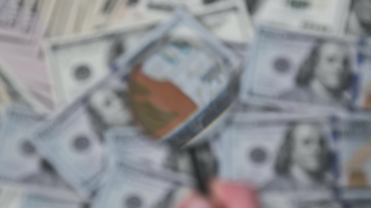 un lote de billetes de cien dólares inspeccionando bajo una lupa