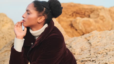 una chica afroamericana posando en piedras junto al mar.