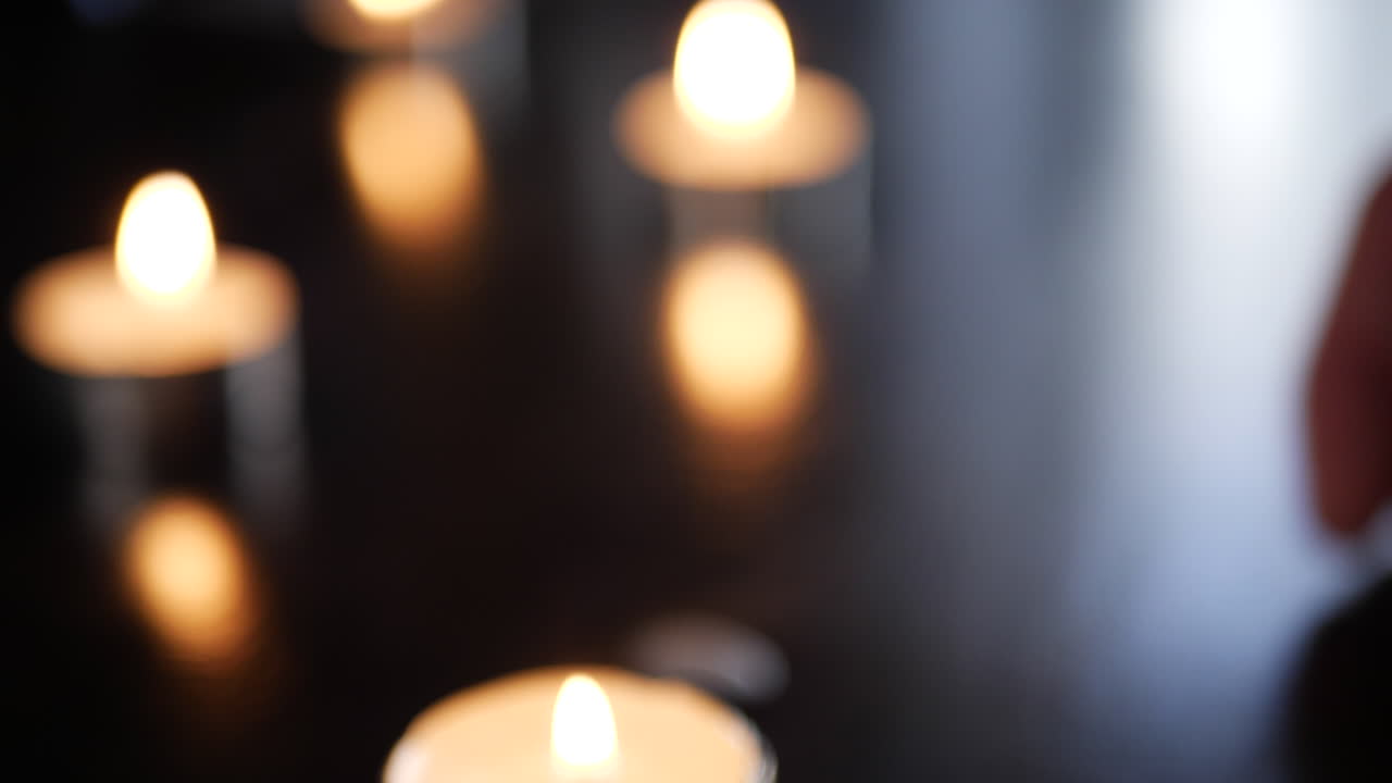 Et sløret baggrundsbillede med en hånd, der placerer fyrfadslys på et bord, og kraftig bokeh under en mindehøjtidelighed eller bøn i en kirke