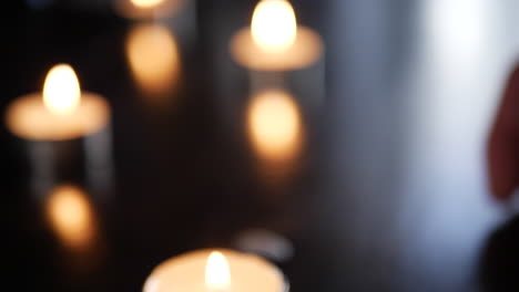 un fondo borroso tomado con una mano colocando velas de candelita en una mesa y un pesado bokeh durante una ceremonia de recuerdo o oración en la iglesia