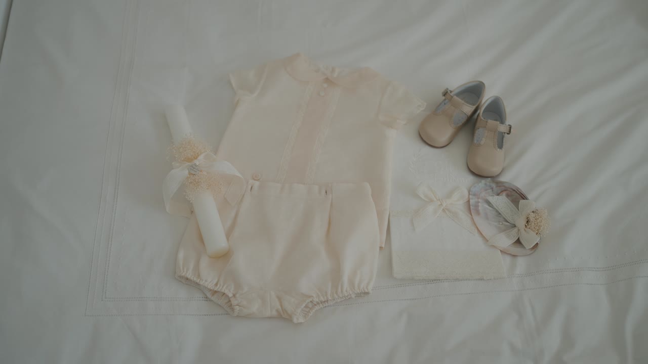 baby christening outfit neatly arranged with matching shoes candle and bonnet on white fabric