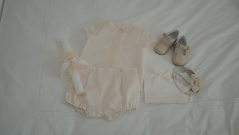 baby christening outfit neatly arranged with matching shoes candle and bonnet on white fabric