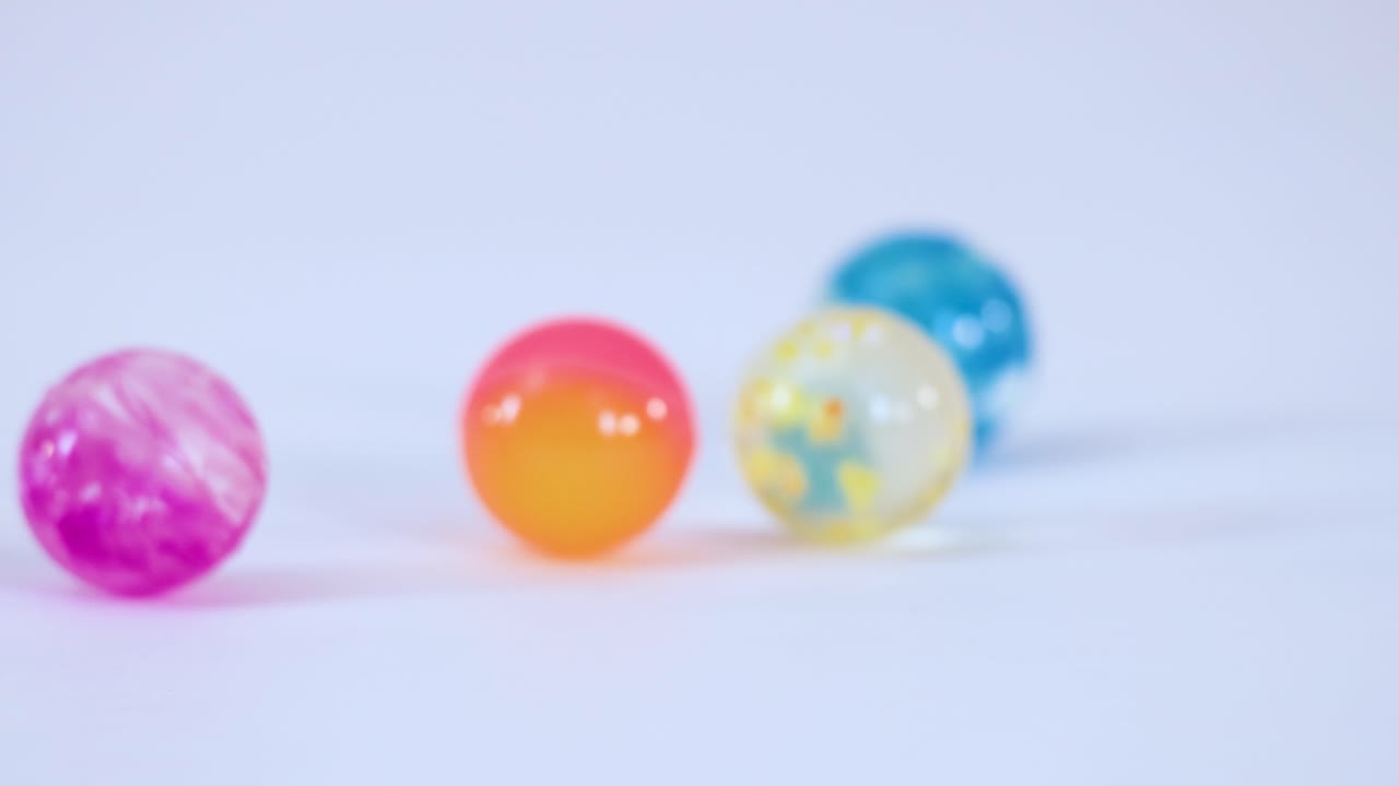 Múltiples pelotas de goma vibrantes rebotan y ruedan sobre una superficie blanca y limpia con iluminación de estudio