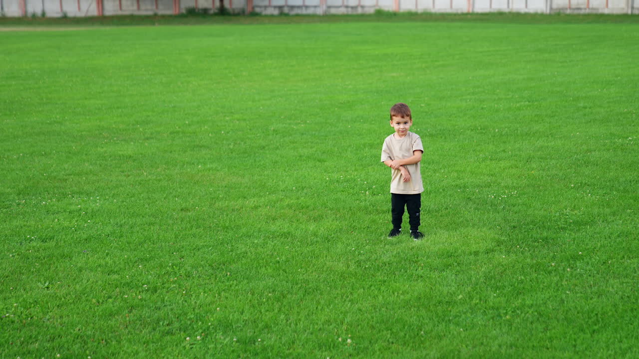Little kid stands on the green lawn. Toddler boy plays cheerfully with a tennis ball outdoors.
