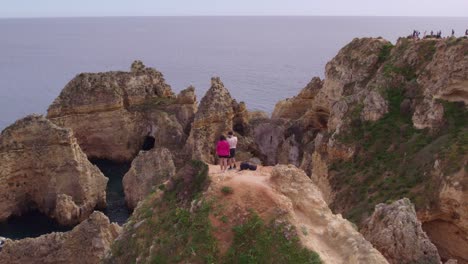 Drone-shot-of-Ponta-da-Piedade-at-Portugal-with-couple-on-edge-of-cliff,-aerial