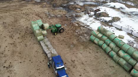 aerial view of tractor unloading round bales from a flatdeck semi truck on a farm in british columbia, canada