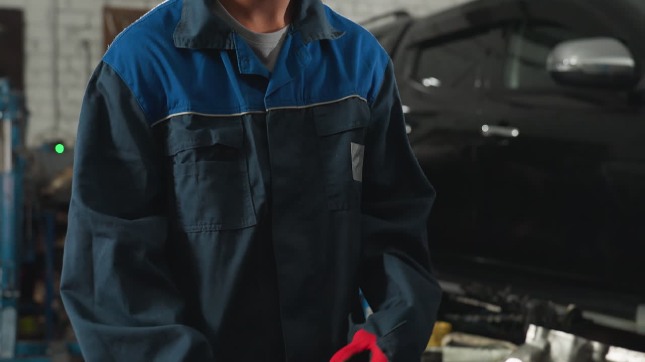 ingeniero en uniforme azul sostiene un raspador mientras trabaja en el motor del coche en el taller de automóviles, el fondo incluye vehículo negro, herramientas mecánicas y equipos de taller