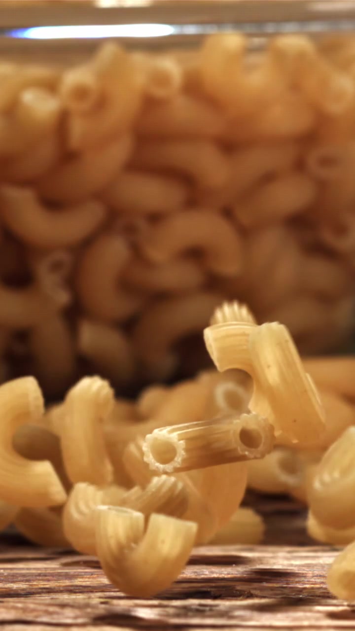 Maccheroni secchi che cadono su una superficie di legno al rallentatore