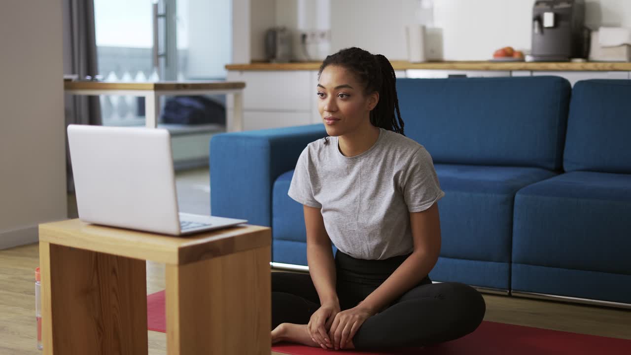 Young woman talking on video call on laptop while sitting on yoga mat