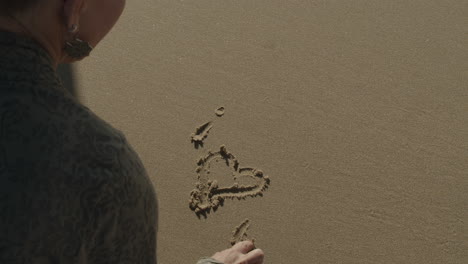 cinematic slow motion shot of woman writing i love you in the sand with her finger
