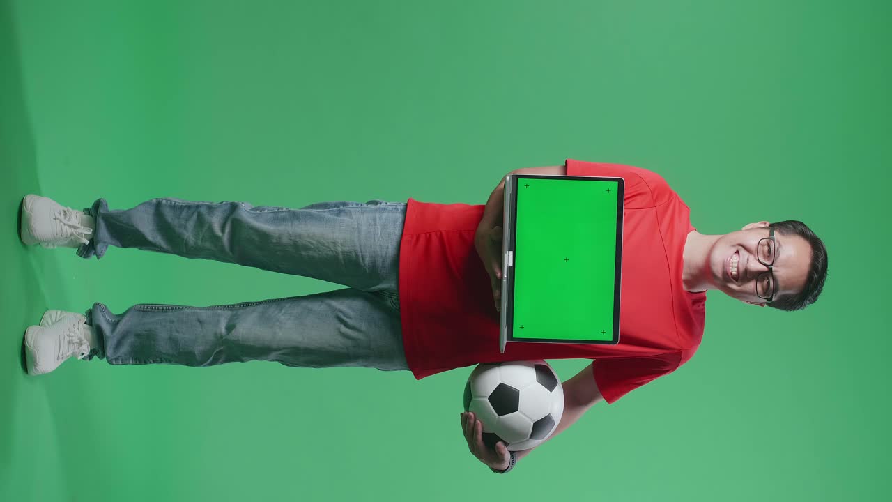 hombre sosteniendo una computadora portátil y una pelota de fútbol frente a la pantalla verde