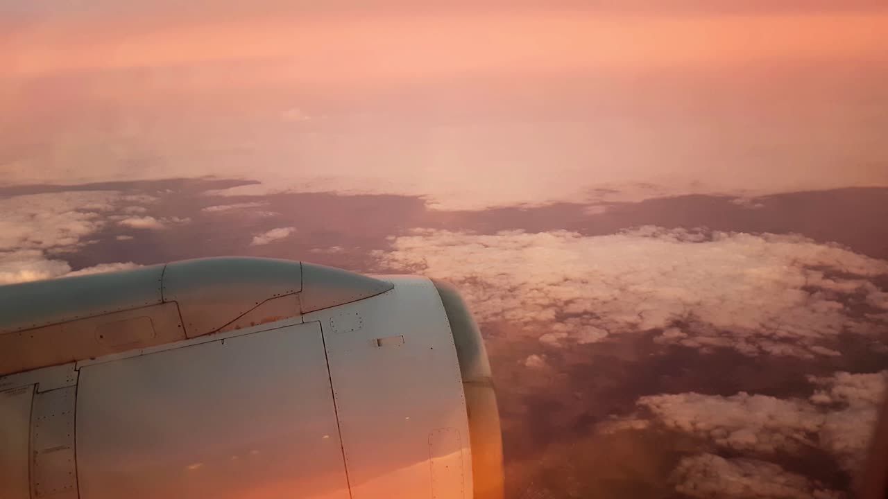 Cielo rosso di notte visto dal finestrino dell'aereo con nuvole sotto e motore a reazione.
