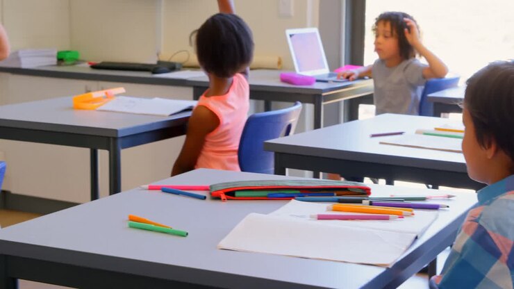Escolares levantando la mano mientras están sentados en el pupitre en la escuela primaria 4k