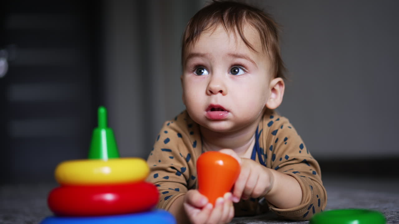 One year old child lies on the floor on his belly. Cute kid holding a toy in little hands and taking it to a mouth. Close up.